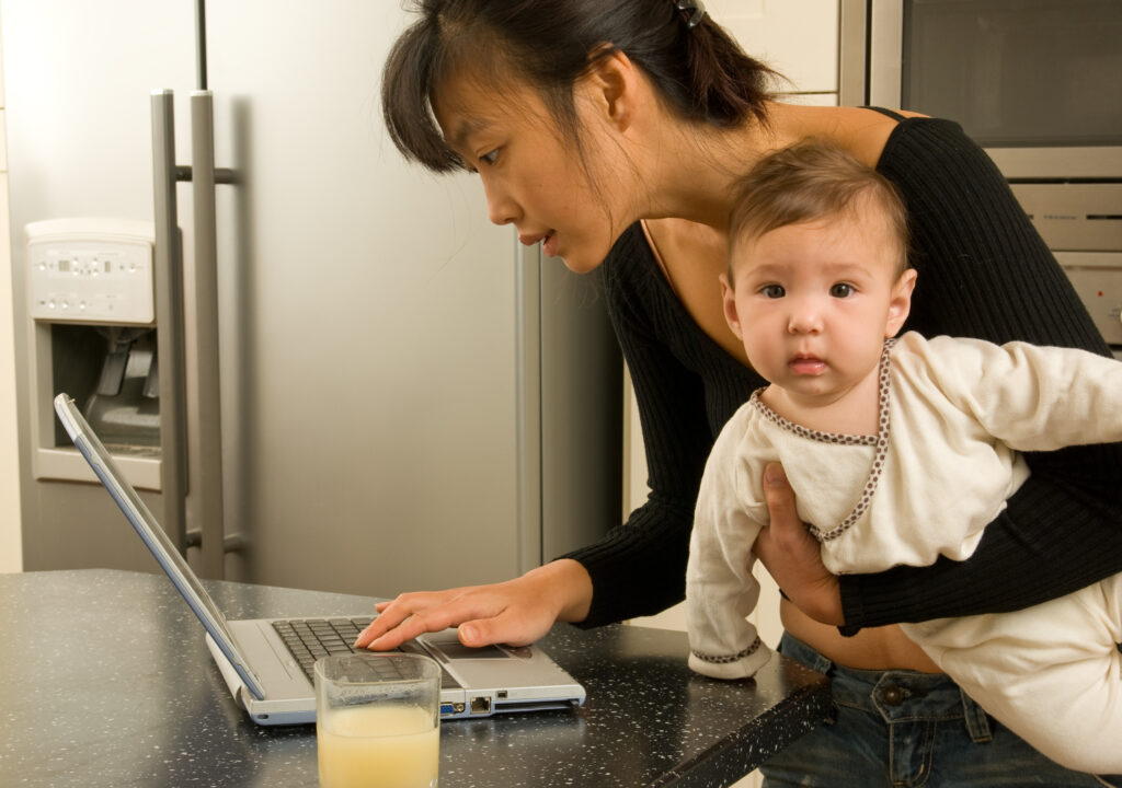 mother working on computer with bored baby mother working on computer with bored baby